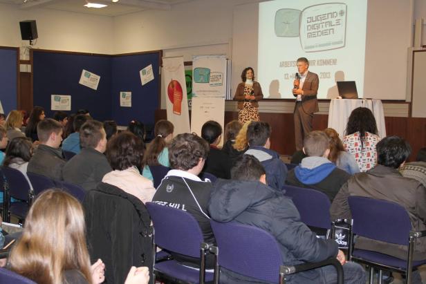 Zwei Personen präsentieren vor einem Publikum zum Thema „Jugend + Digitale Medien“.