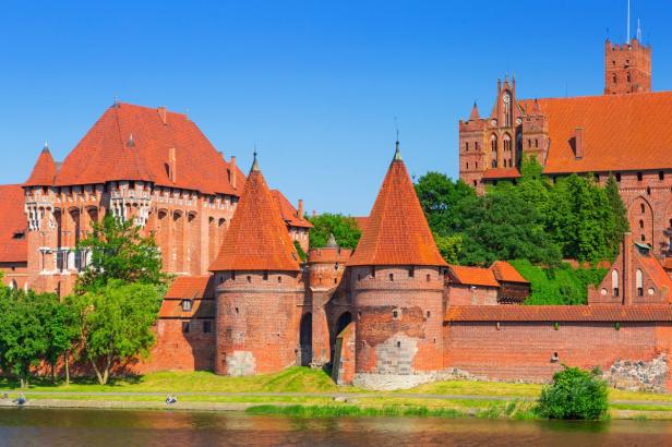 Die Marienburg in Polen mit ihren roten Backsteingebäuden und Türmen am Flussufer.
