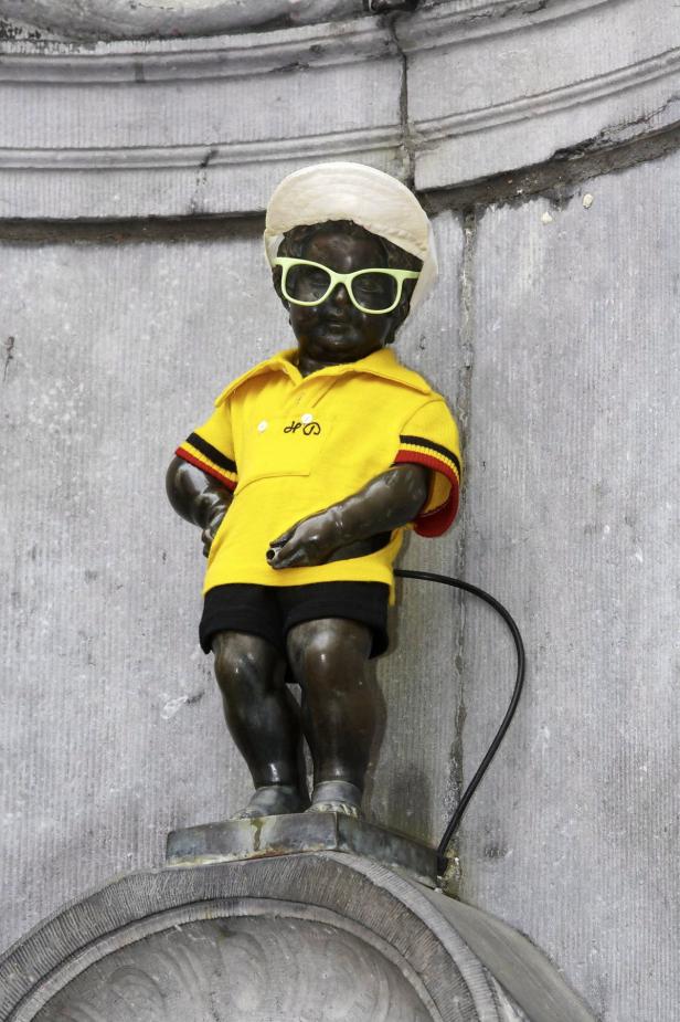 Die Manneken-Pis-Statue in Brüssel trägt einen Hut, eine Sonnenbrille und ein gelbes T-Shirt.