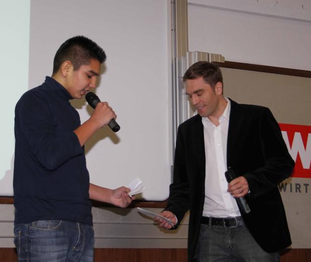 Ein junger Mann spricht in ein Mikrofon, während ein anderer Mann ihm zuhört.