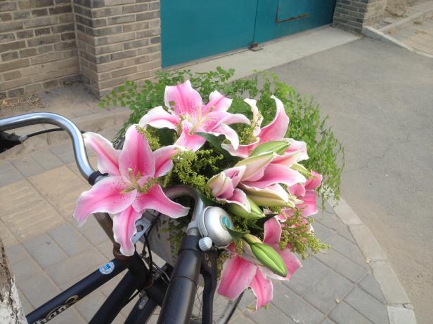 Ein Fahrradkorb ist mit rosa Lilien und Grünzeug gefüllt.
