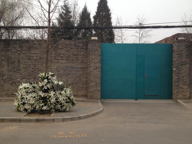 Ein großer Strauß weißer Lilien steht vor einer türkisfarbenen Tür und einer Backsteinmauer.