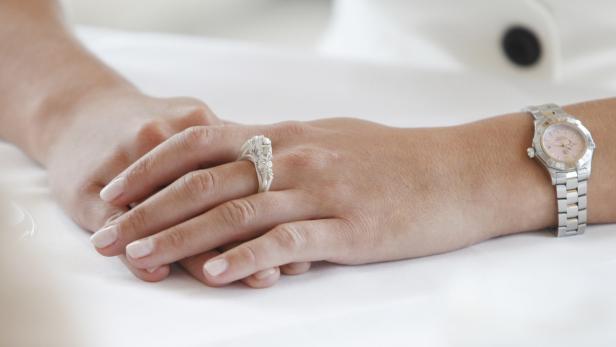 Die Hände einer Frau mit einem auffälligen Ring und einer silbernen Armbanduhr liegen auf einem Tisch.