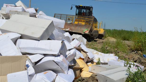 Ein gelber Bulldozer schiebt einen Haufen von Kartons auf einem Feld zusammen.