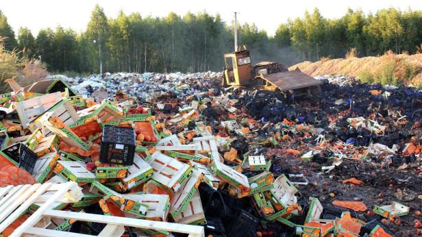 Eine Mülldeponie mit Obstkisten, Plastikmüll und einem Bulldozer im Hintergrund.