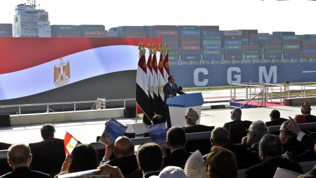 Ägyptischer Präsident hält eine Rede vor Flaggen und einem Containerschiff.