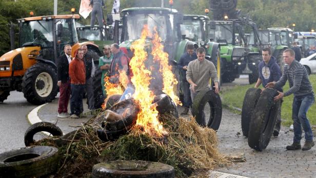 Bauern protestieren mit brennenden Reifen und Traktoren im Hintergrund.