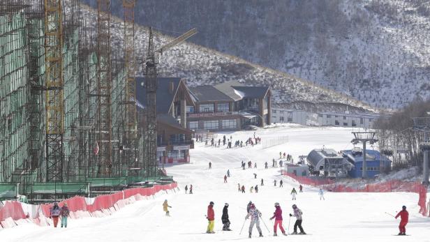 Auf einer Skipiste fahren Menschen Ski, im Hintergrund Gebäude und ein unfertiges Bauwerk.