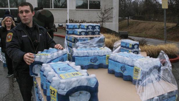 Ein Feuerwehrmann hantiert mit Paletten von Wasserflaschen vor einem Gebäude.