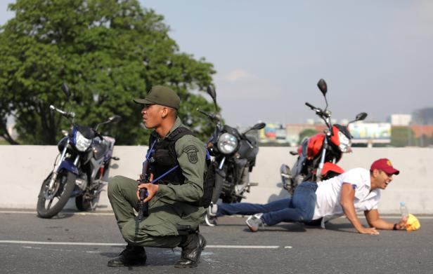 A military member and a man take cover near the Generalisimo Francisco de Miranda Airbase in Caracas