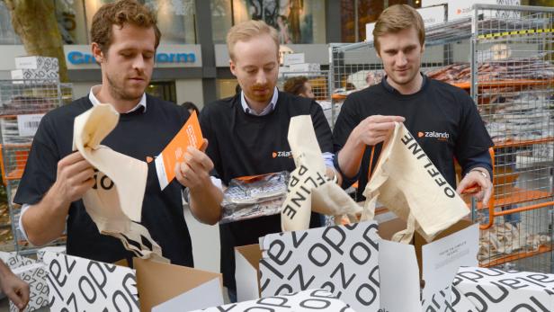 Drei Männer in schwarzen Zalando-T-Shirts packen Stoffbeutel in Kartons.