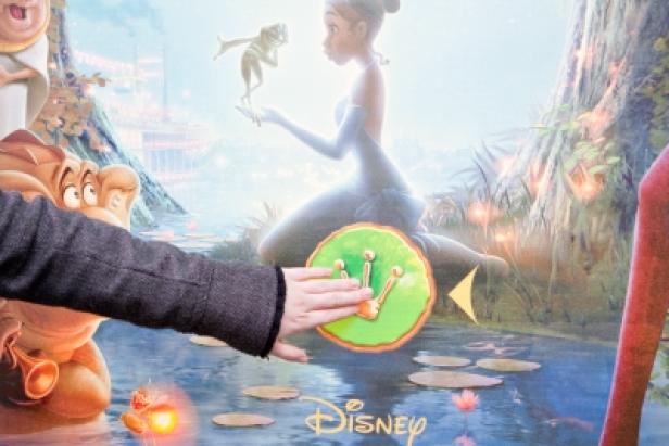Eine Person berührt eine interaktive Darstellung von Tiana und dem Frosch.