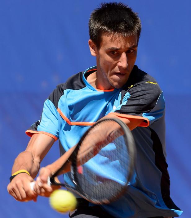 Ein Tennisspieler schlägt einen gelben Tennisball vor einem blauen Hintergrund.