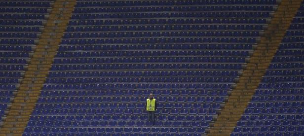 Ein Ordner steht in einem leeren Stadion mit blauen Sitzen.