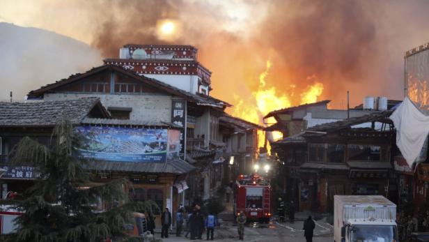 Ein Brand wütet in einer Stadt mit traditioneller Architektur, während Feuerwehrleute versuchen, ihn zu löschen.