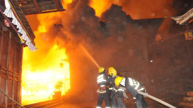 Feuerwehrleute bekämpfen einen Brand in einem Gebäude mit traditioneller Architektur.