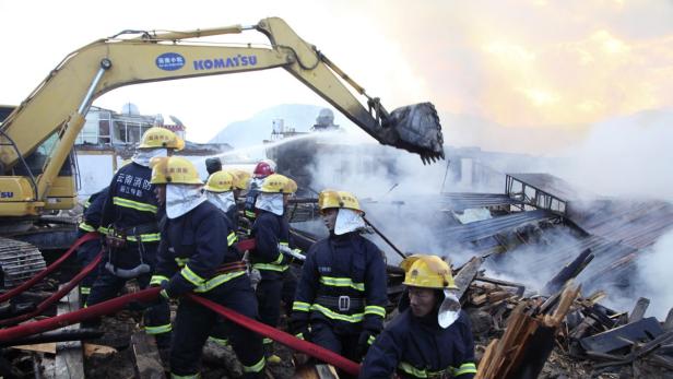 Feuerwehrleute bekämpfen einen Brand mit einem Bagger und Wasserwerfern.