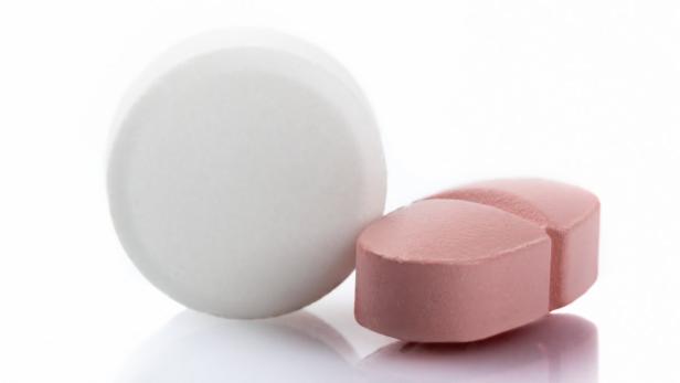 Eine weiße, runde Tablette und eine rosafarbene, längliche Tablette liegen nebeneinander.