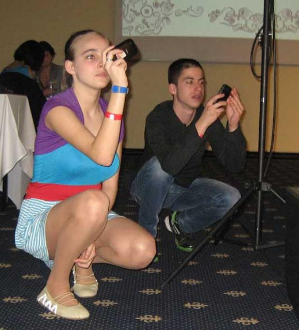 Eine junge Frau und ein junger Mann hocken und fotografieren mit ihren Handys.