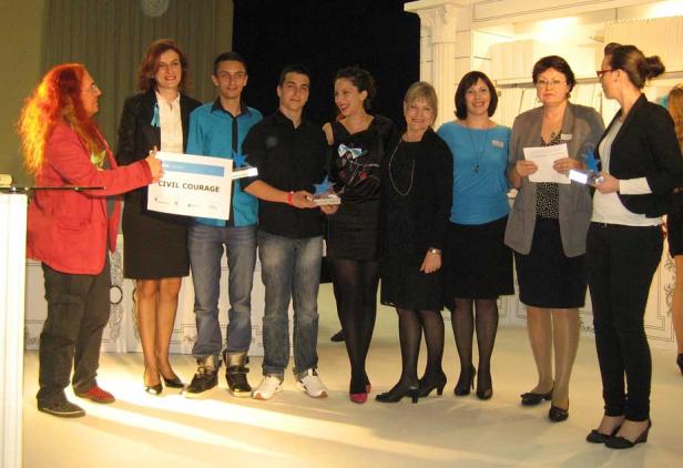 Eine Gruppe von Personen steht auf einer Bühne und hält eine Auszeichnung mit der Aufschrift „Civil Courage“.