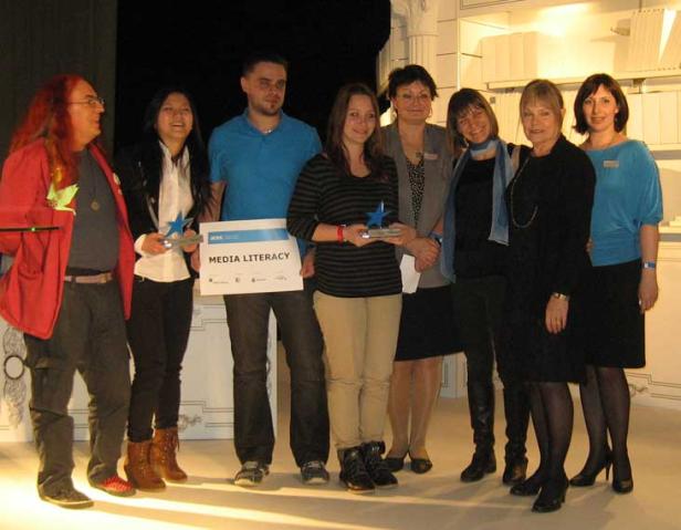 Eine Gruppe von Personen posiert mit einem „Media Literacy“-Schild und Stern-Trophäen.