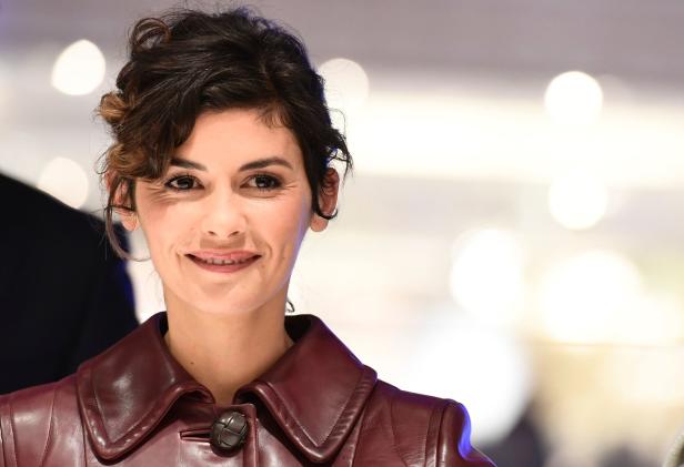 Audrey Tautou lächelt in einer bordeauxroten Lederjacke.