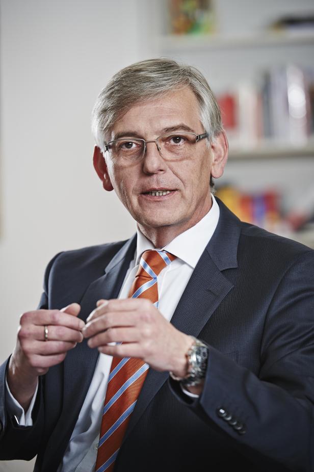 Ein Mann mit Brille, Anzug und Krawatte sitzt in einem Büro.