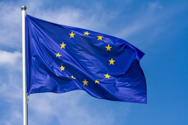 Flag of the European Union waving in the wind on flagpole against the sky with clouds