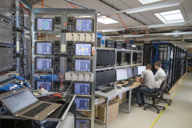 In einem Serverraum arbeiten zwei Personen an Computern vor mehreren Serverschränken.