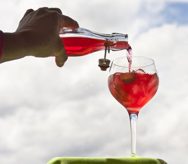Eine Hand gießt ein rotes Getränk aus einer Flasche in ein Weinglas.