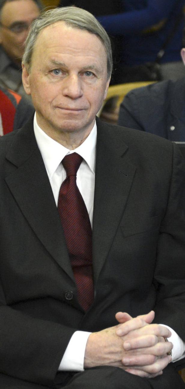 Ein Mann im Anzug sitzt mit verschränkten Händen da.