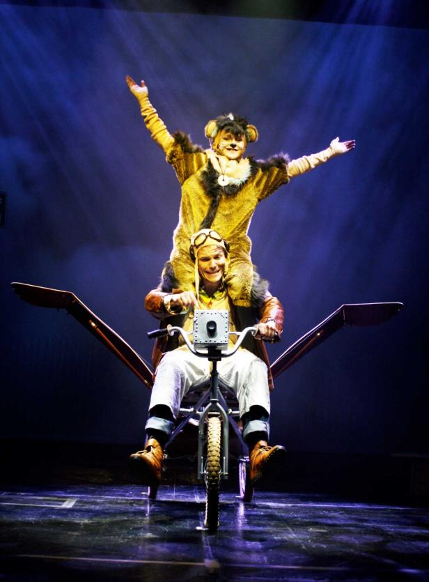 Zwei Darsteller in Kostümen auf einer Art Fahrrad-Flugzeug-Bühnenrequisite.