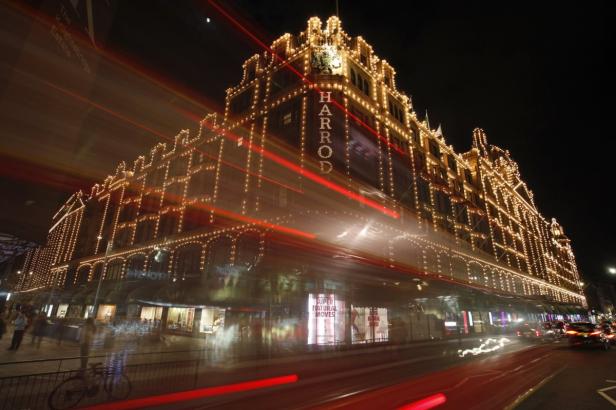 Das beleuchtete Harrods-Kaufhaus in London bei Nacht mit verwischten Lichtern vorbeifahrender Autos.