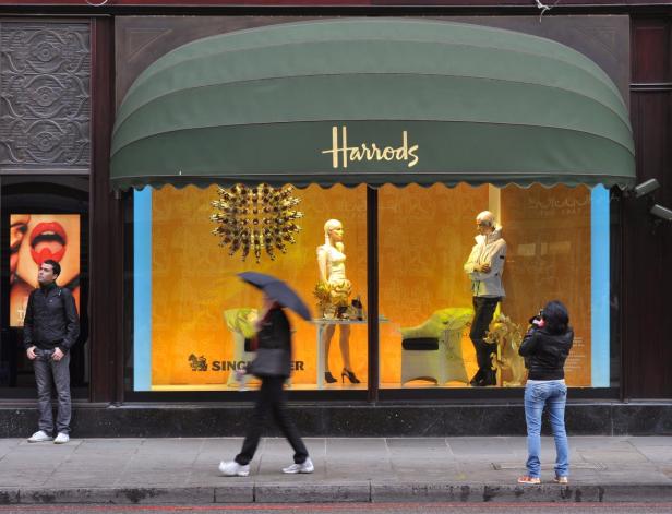 Ein Schaufenster von Harrods mit zwei Schaufensterpuppen und Passanten.