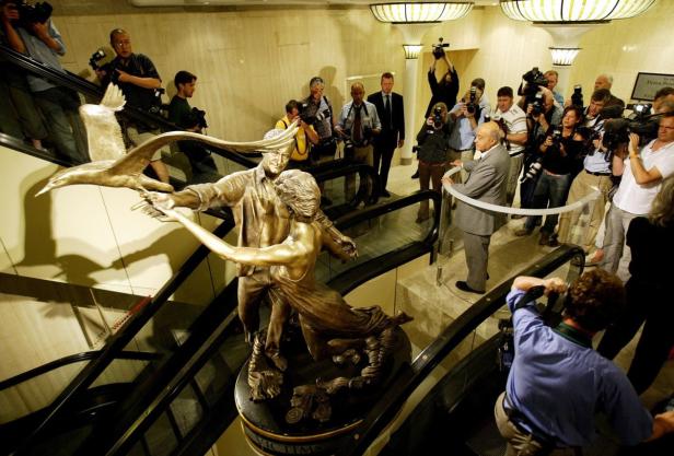 Eine Bronzestatue von Diana und Dodi auf einer Rolltreppe, umringt von Fotografen.