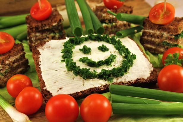 Ein Brot mit Frischkäse und einem Smiley aus Schnittlauch, umgeben von Tomaten und Frühlingszwiebeln.