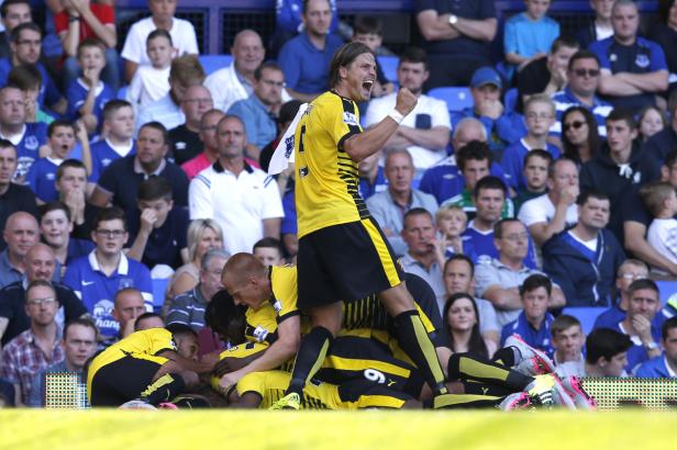 Jubelnde Fußballspieler in gelb-schwarzen Trikots liegen übereinander vor einer Zuschauermenge.