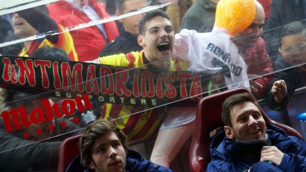 Lionel Messi sitzt auf der Tribüne, während Fans hinter einer Glasscheibe zu sehen sind.