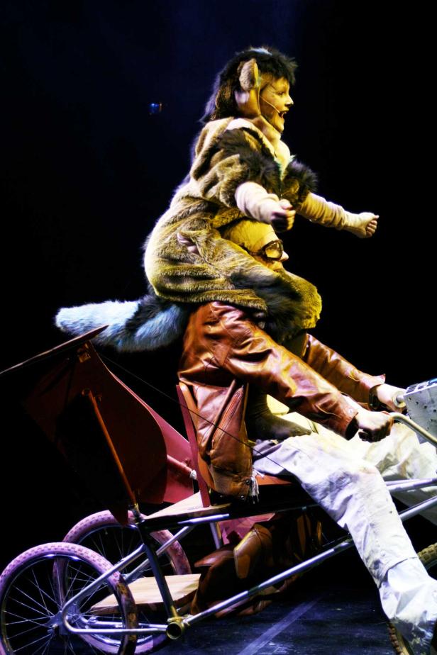 Zwei Personen in Kostümen fahren auf einer Art Fahrradkonstruktion.