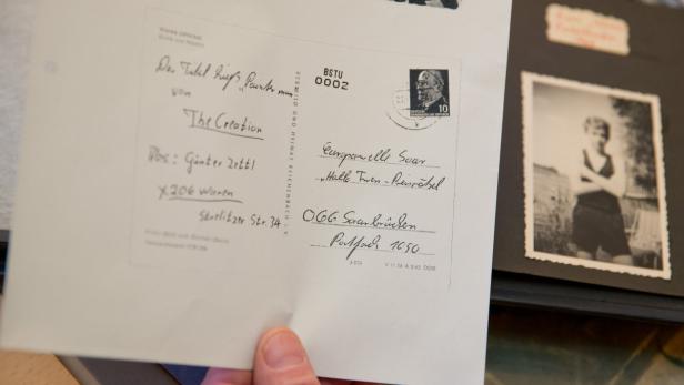 Eine alte Postkarte mit einer Briefmarke und handschriftlichen Notizen liegt neben einem Fotoalbum.