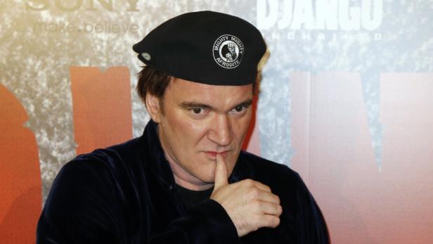 Quentin Tarantino mit einer schwarzen Baskenmütze vor einem „Django Unchained“-Poster.