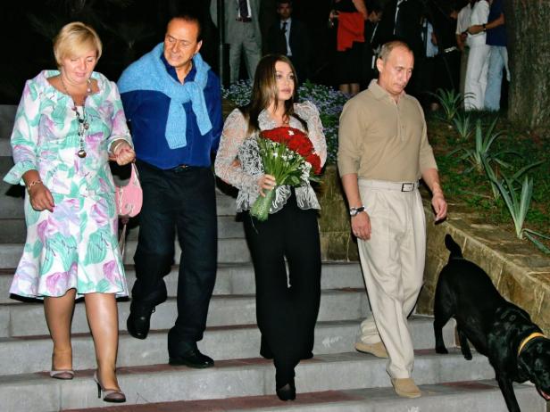 Silvio Berlusconi, Wladimir Putin und Begleiter steigen eine Treppe hinunter, begleitet von einem schwarzen Hund.