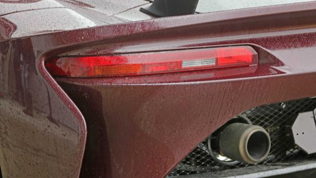 Nahaufnahme des Rücklichts und Auspuffs eines bordeauxroten Autos.
