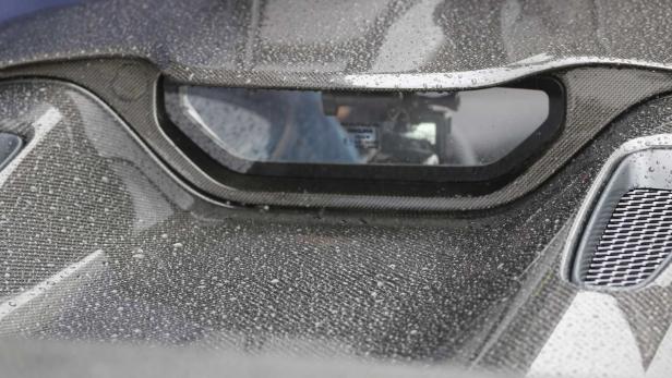 Detailansicht der Carbonfaser-Karosserie eines Autos mit Wassertropfen und einem kleinen Fenster.