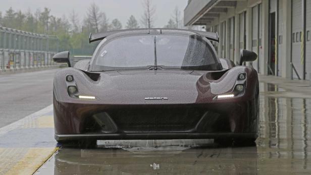 Ein dunkelroter, sportlicher Wagen steht im Regen auf einer Rennstrecke.