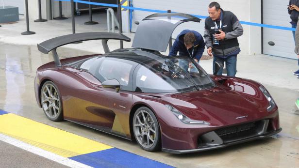 Ein dunkelroter Dallara-Sportwagen mit Flügeltüren steht auf einer Rennstrecke.