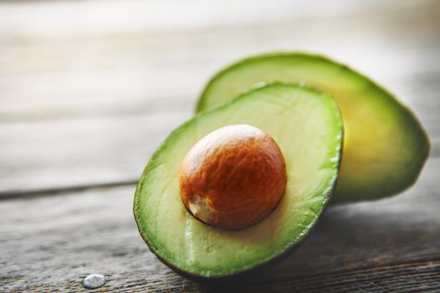 Eine halbierte Avocado mit großem Kern liegt auf einer Holzfläche.