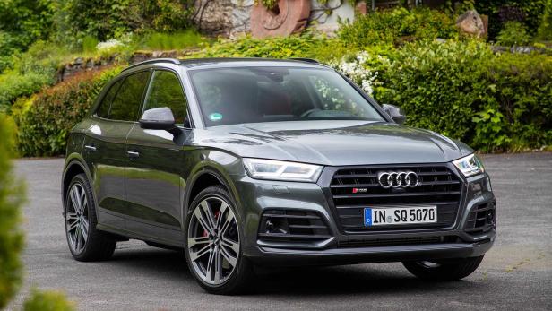Ein grauer Audi SQ5 steht vor einer grünen Hecke.