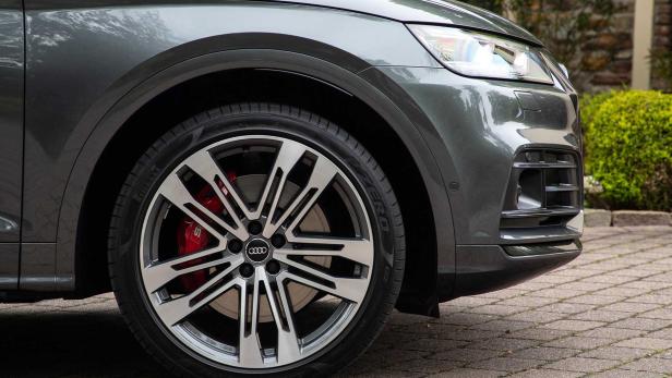 Detailansicht eines grauen Audi mit markanten Felgen und roten Bremssätteln.