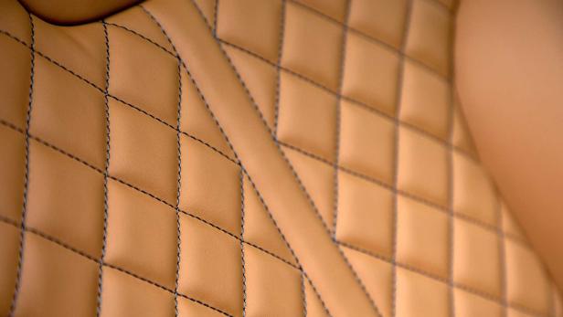 Detailaufnahme von gestepptem, hellbraunem Leder mit dunklen Ziernähten.